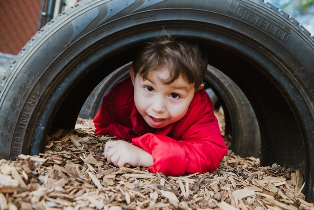 Boy crawling under a tire at Bissell's outdoor play area.